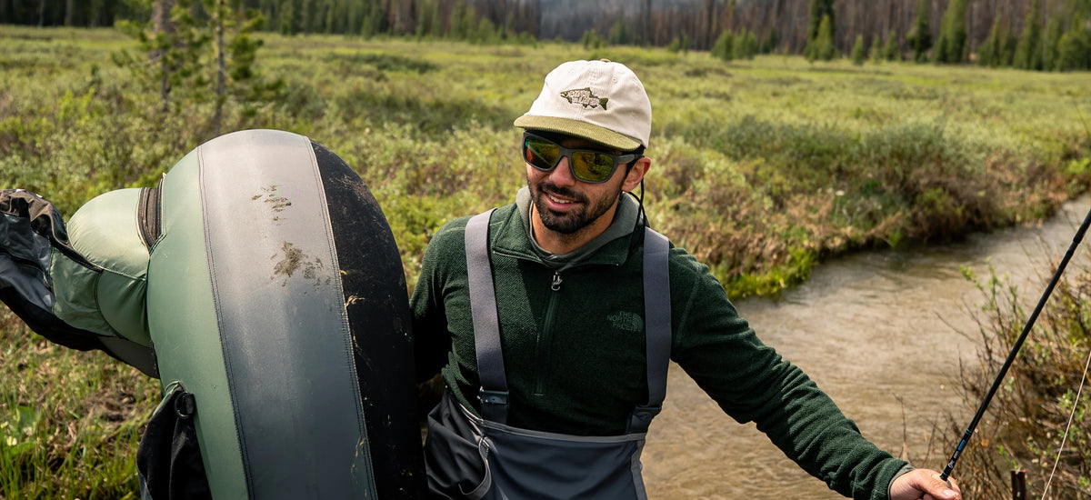 Fly fishing angler, crossing a creek with a fly rod and outcast float tube with a mountain backdrop.